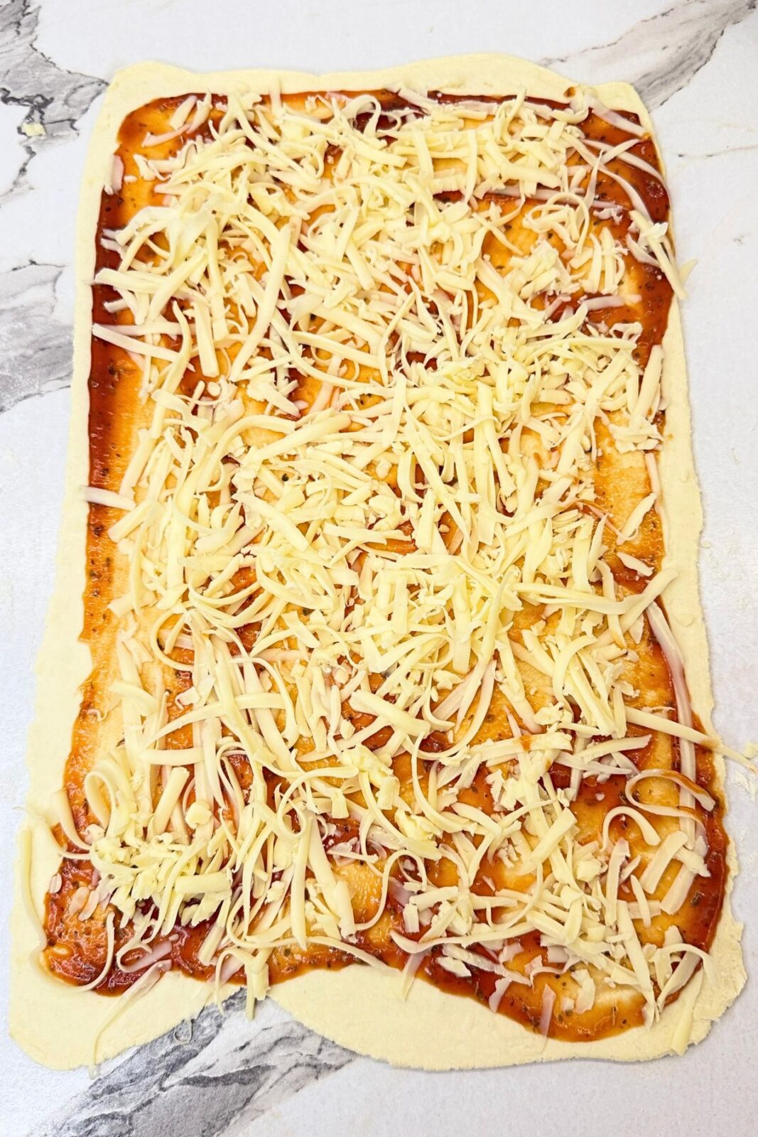 Puff pastry topped with pizza sauce and shredded cheese before rolling into pizza rolls.