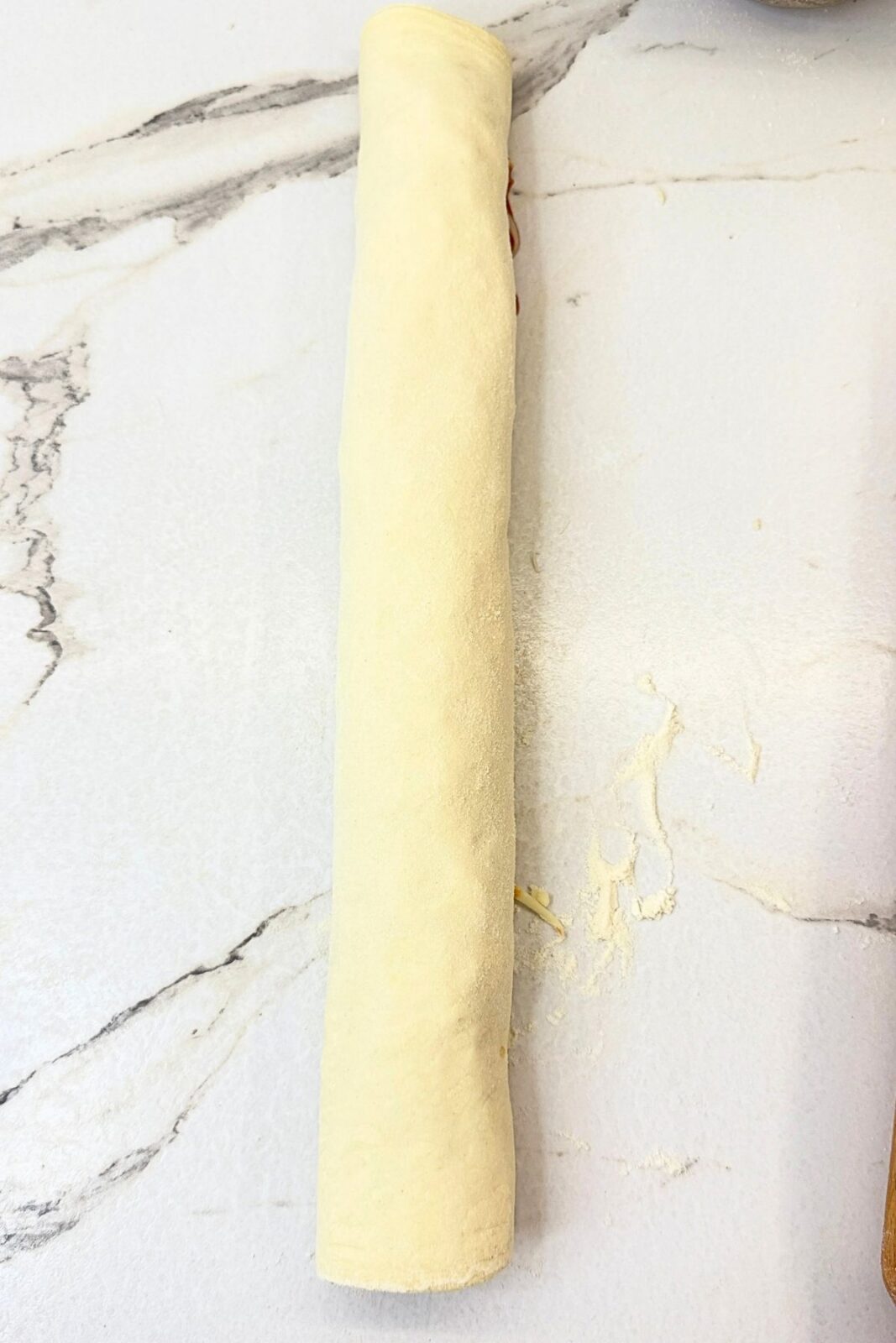 Puff pastry rolled into a log with pizza sauce and cheese filling, ready to slice.