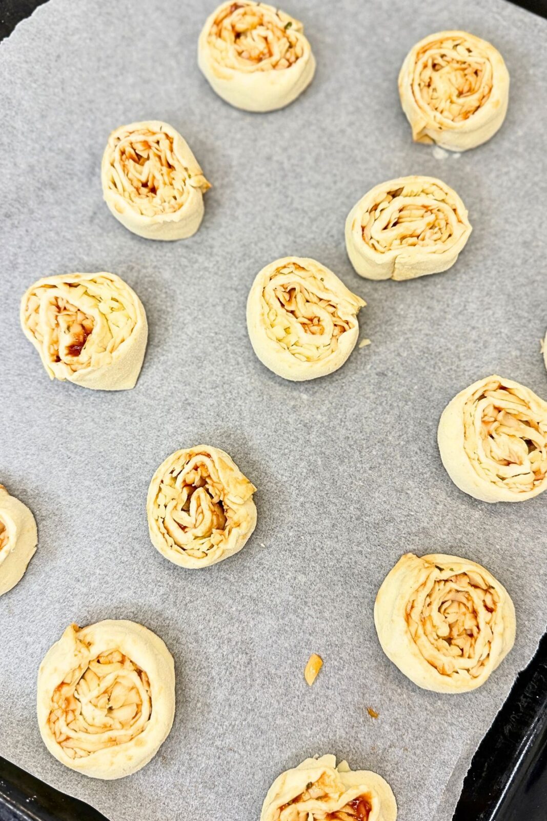 Unbaked pizza rolls arranged cut-side up on a parchment-lined baking sheet.