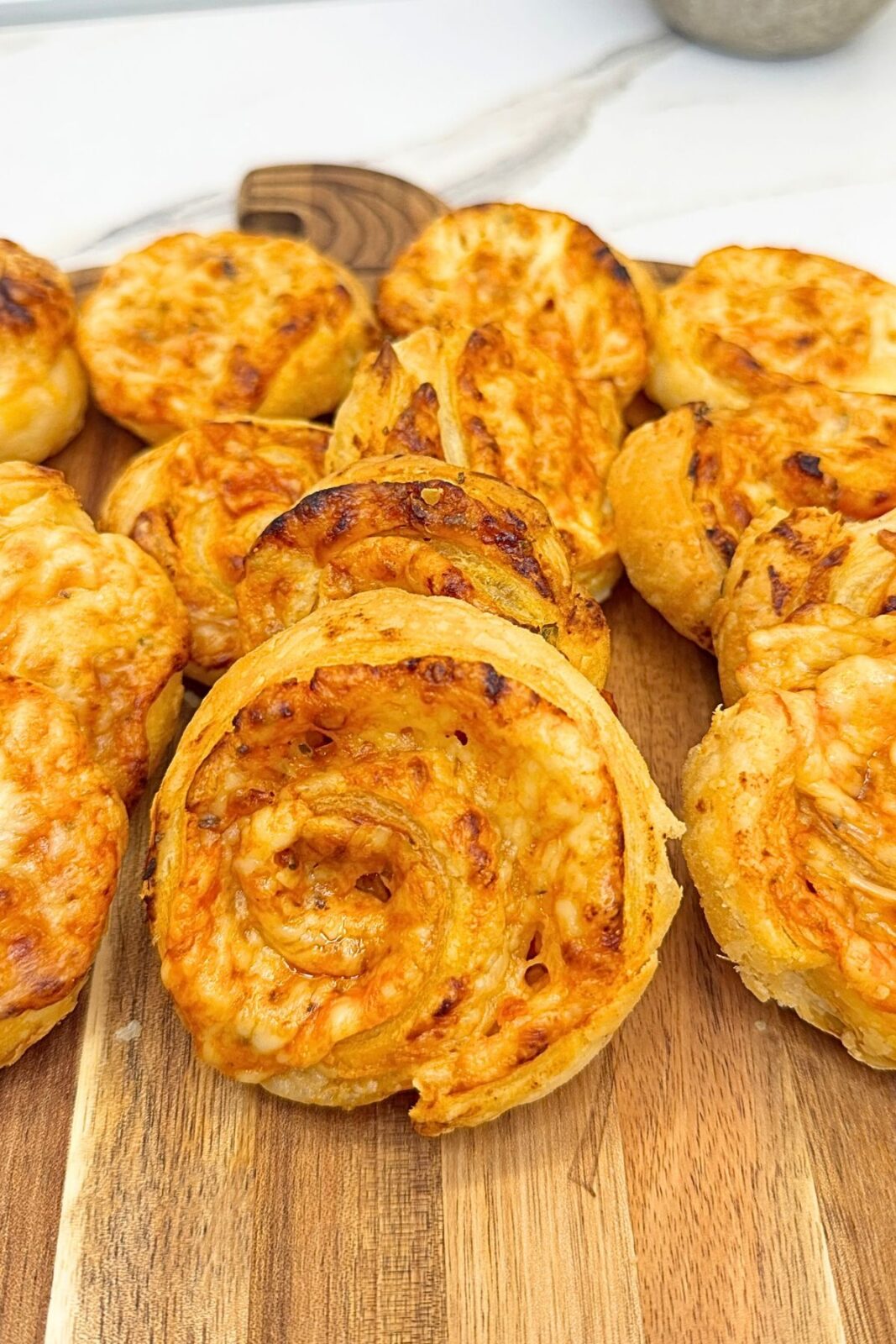 Freshly baked pizza rolls with golden puff pastry and melted cheese on a wooden serving board.