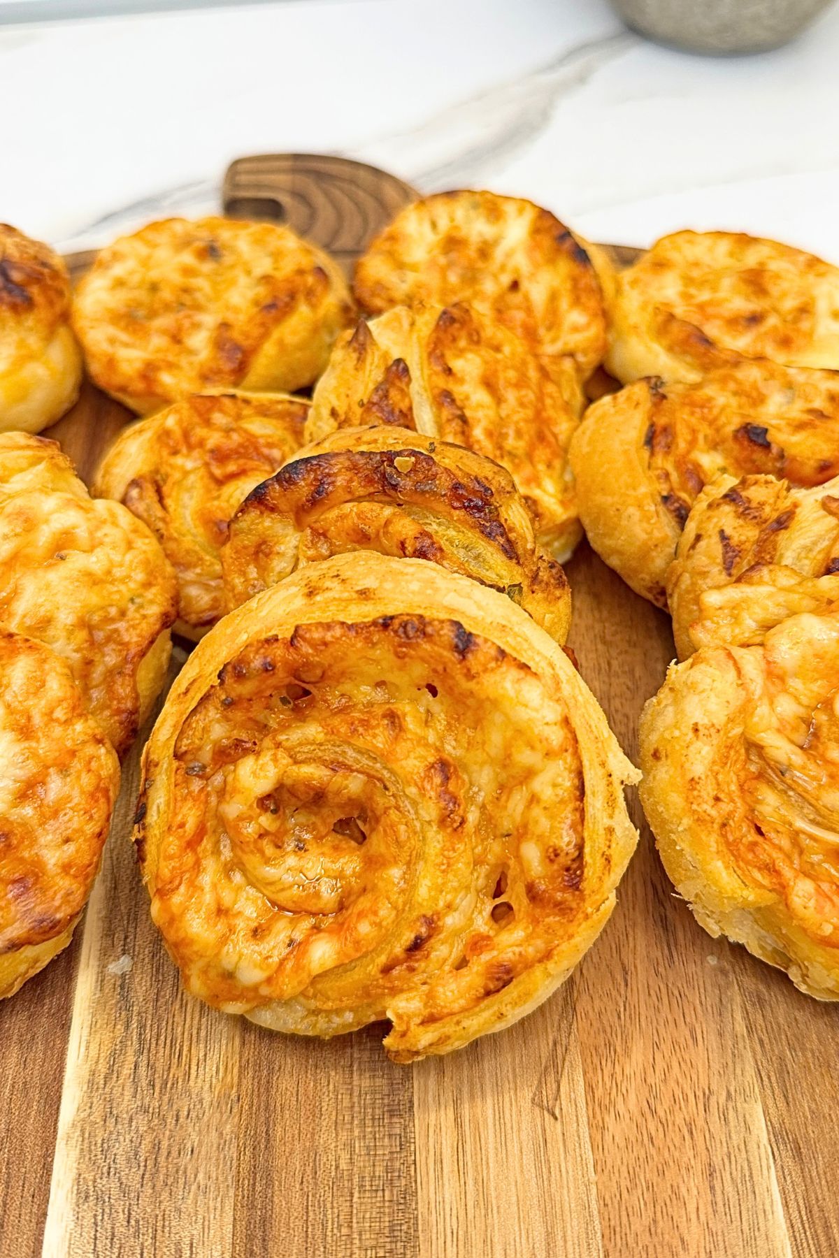 Golden puff pastry pizza rolls filled with melted cheese and pizza sauce on a ceramic platter, with a bowl of pizza sauce on the side.