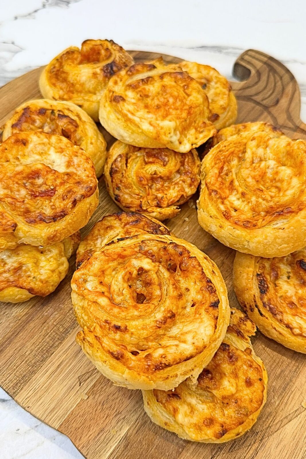 Golden puff pastry pizza rolls filled with cheese and pizza sauce, stacked on a wooden serving board.