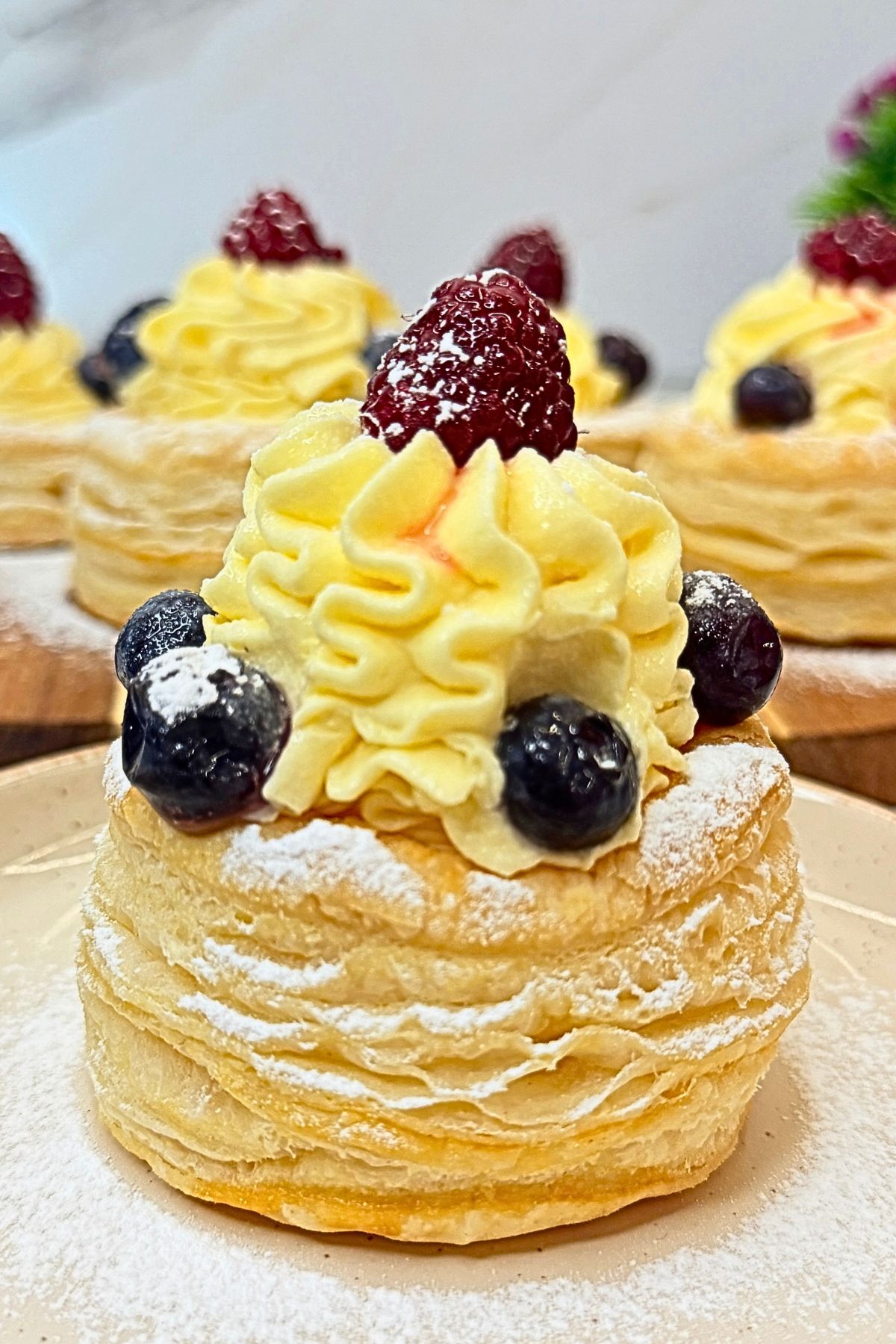 Puff pastry cups filled with vanilla cream, topped with blueberries and raspberries, and dusted with powdered sugar.
