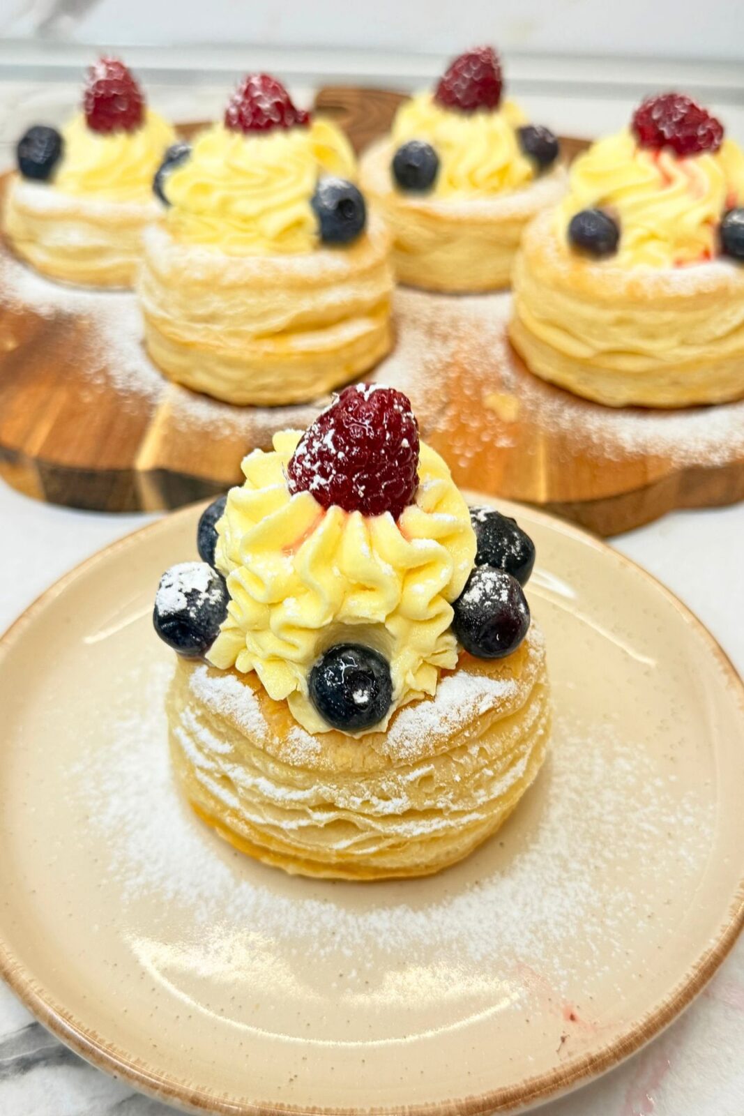 Finished puff pastry cups filled with vanilla cream, topped with blueberries and raspberries, and dusted with powdered sugar.