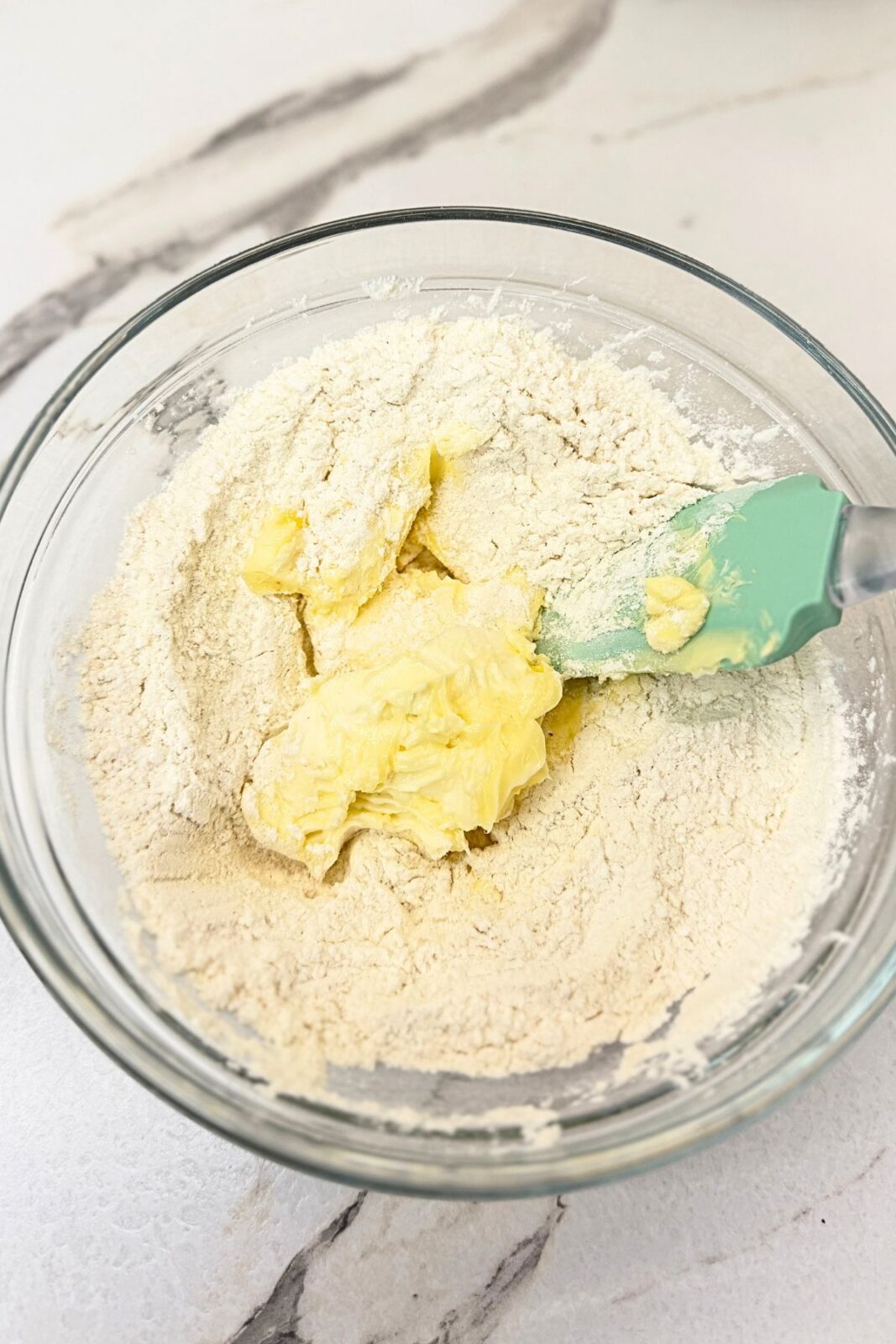 Butter and dry ingredients in a glass mixing bowl with a spatula, ready to make vanilla crescent cookie dough.