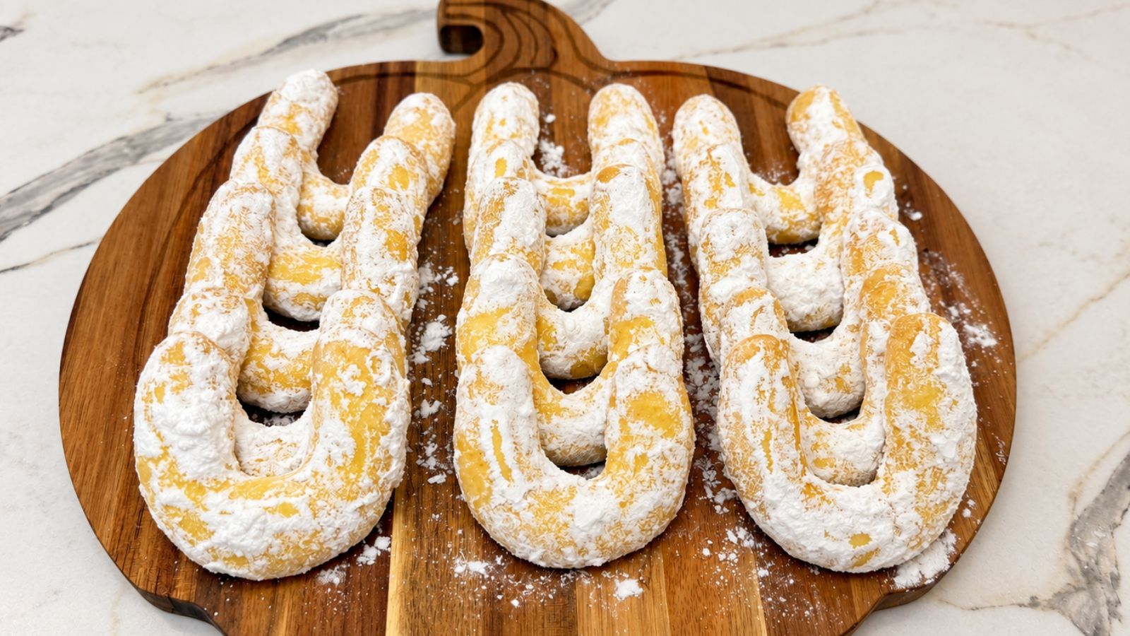 Vanilla crescent cookies made with pudding mix, coated in powdered sugar and arranged on a round wooden serving board.