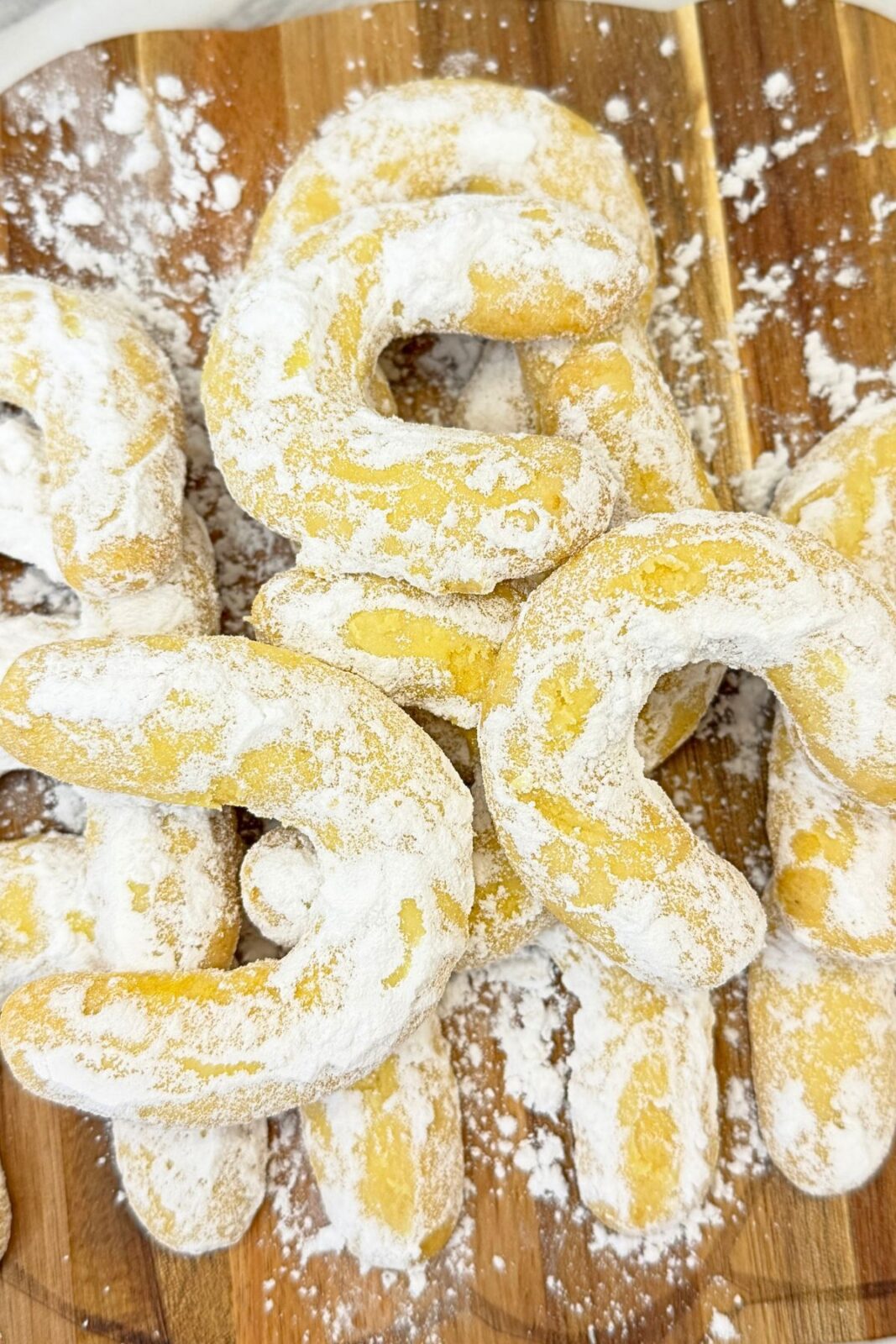 Vanilla crescent cookies coated in powdered sugar, stacked on a wooden serving board and viewed from above.