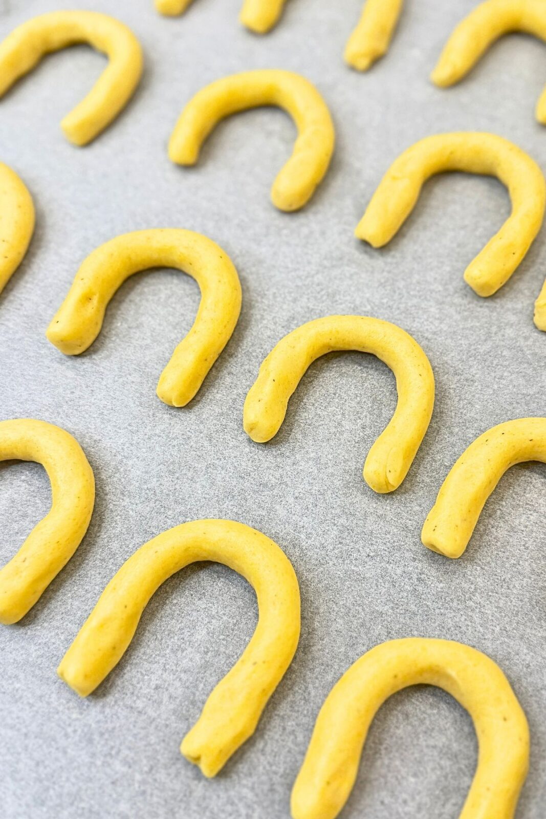 Unbaked vanilla crescent cookies arranged on a parchment-lined baking sheet.