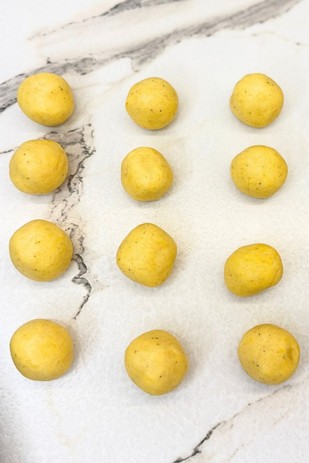 Vanilla crescent cookie dough divided into small balls on a marble work surface.
