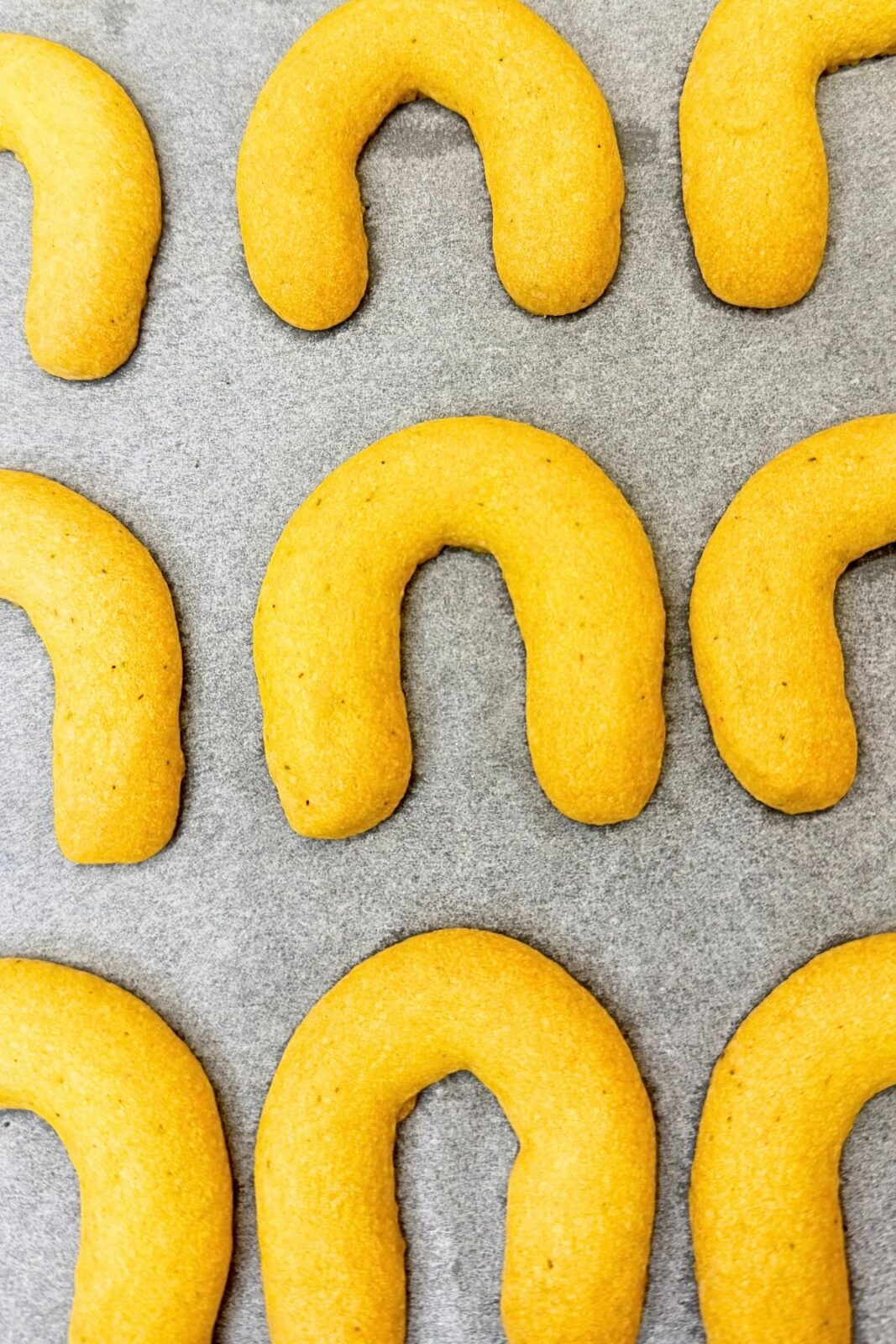 Baked vanilla crescent cookies on parchment paper before coating in powdered sugar.