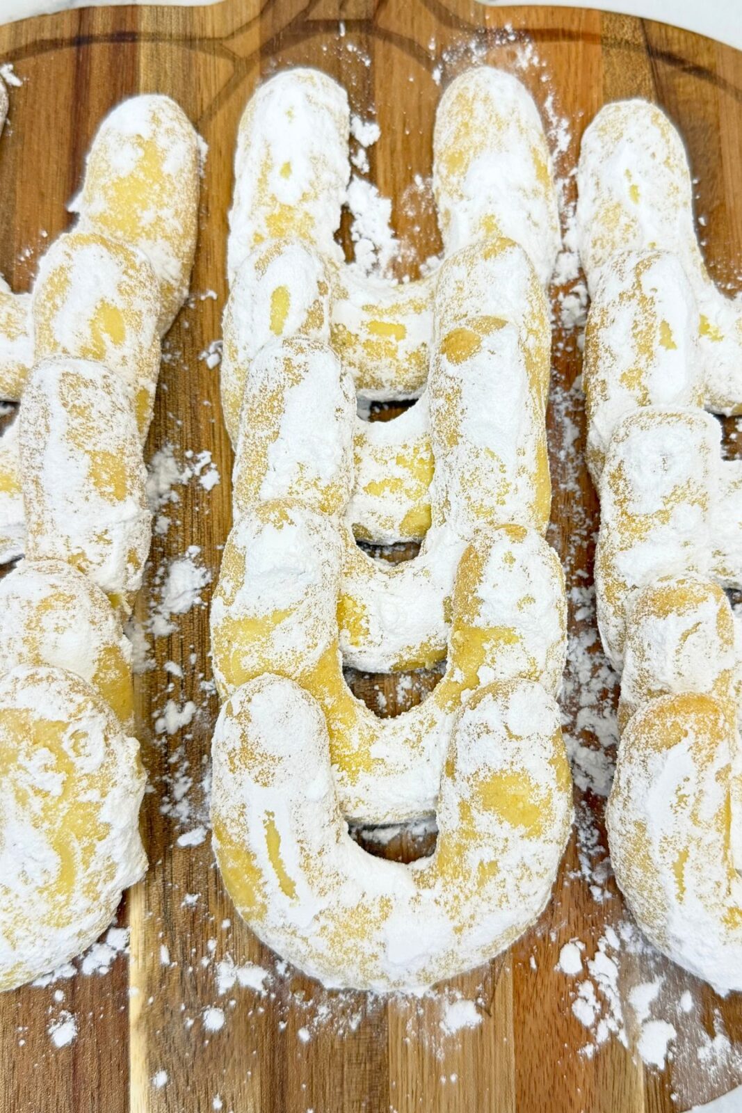 Close-up of vanilla crescent cookies coated in powdered sugar on a wooden serving board.