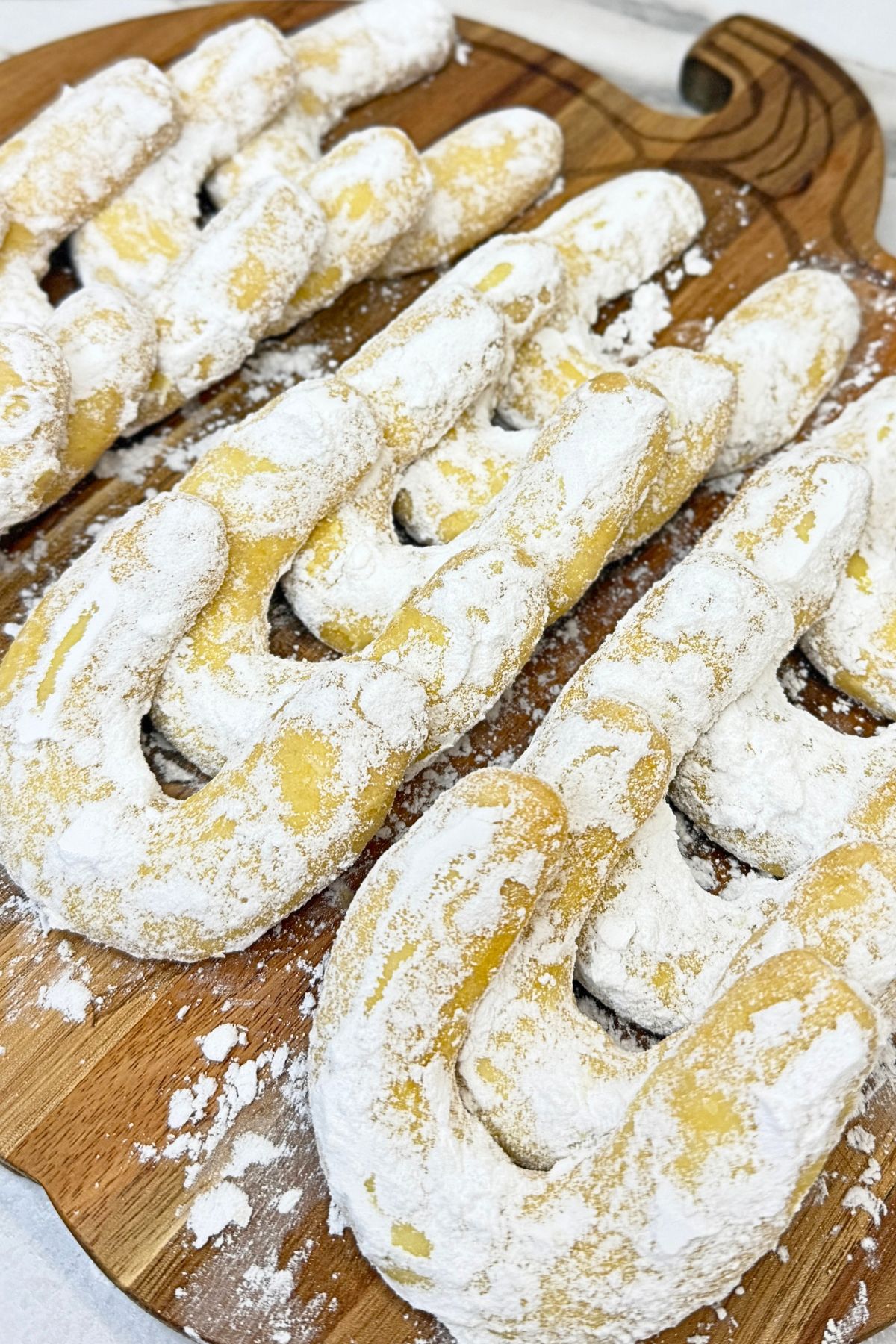 Vanilla crescent cookies made with pudding mix, coated in powdered sugar and arranged on a round wooden serving board.