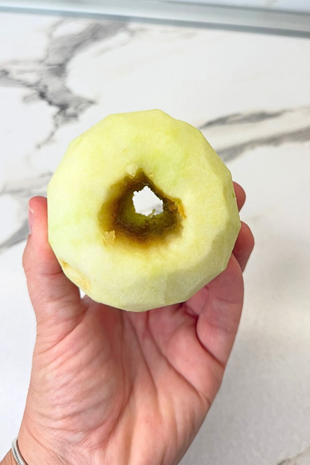Peeled Granny Smith apple held in one hand, showing the hollow center prepared for walnut filling.