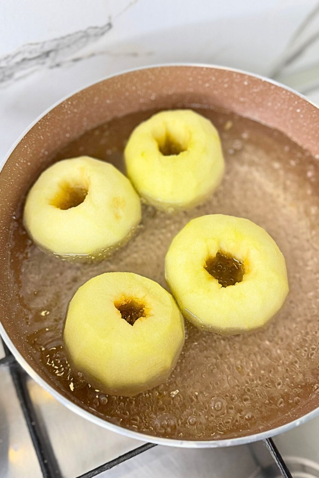 Four peeled and cored Granny Smith apples simmering in sugar syrup for walnut stuffed apples.