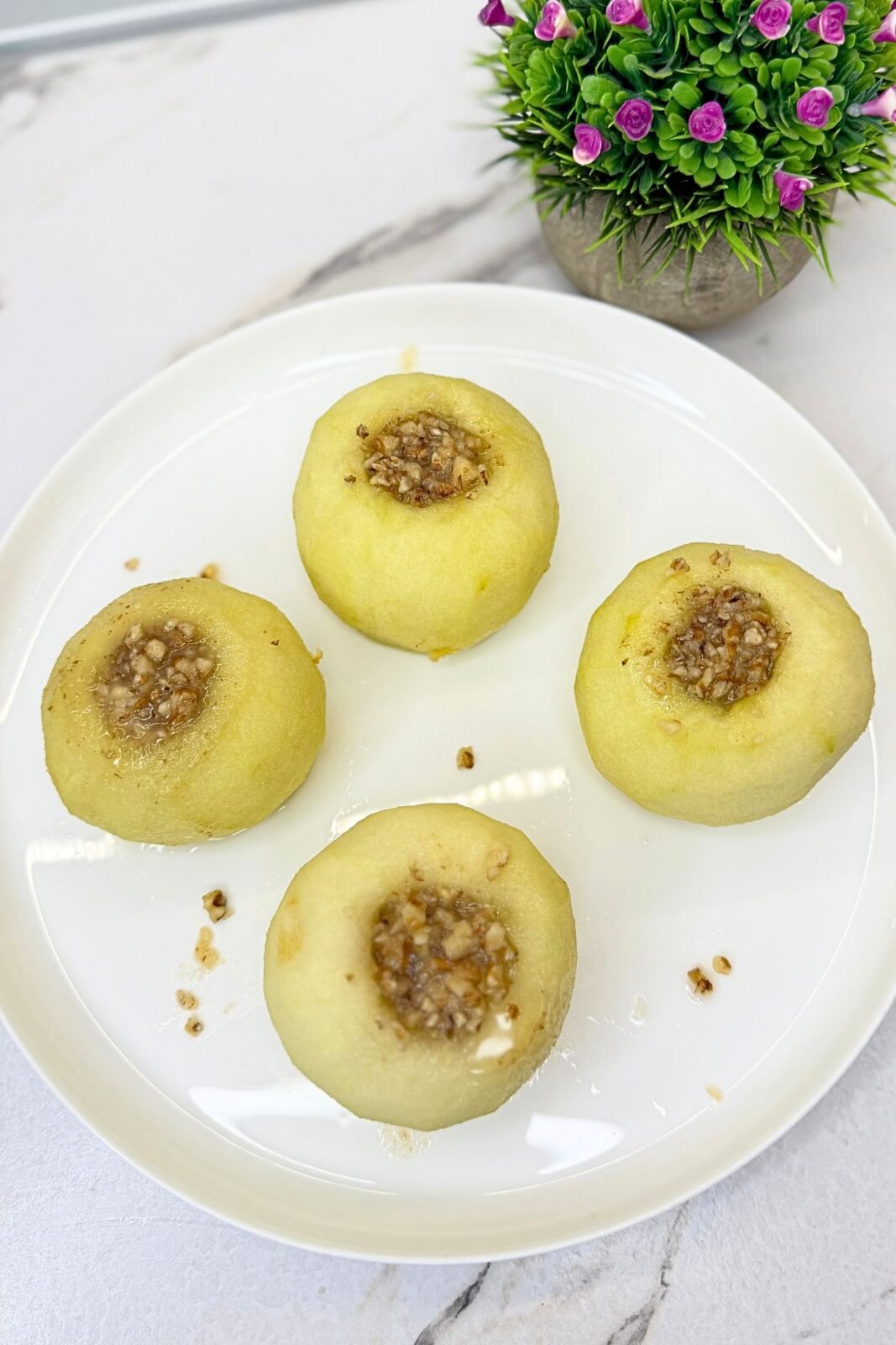 Four walnut stuffed apples on a white platter, showing the walnut and syrup filling before decorating.