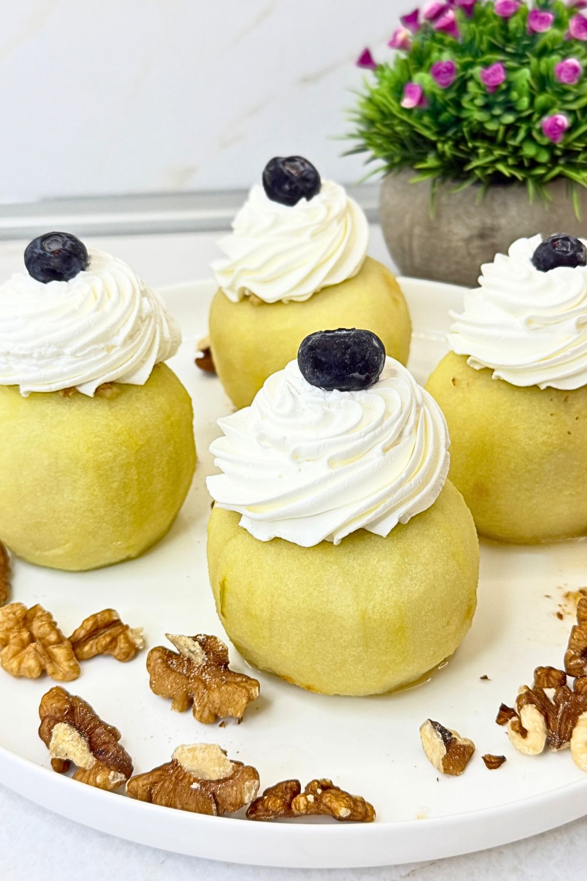 Walnut stuffed apples topped with whipped cream and blueberries on a white platter with scattered walnuts.